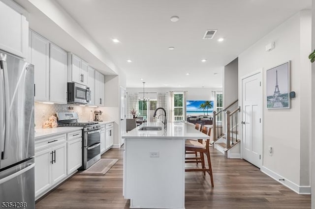 kitchen featuring appliances with stainless steel finishes, a breakfast bar, a sink, a kitchen island with sink, and visible vents