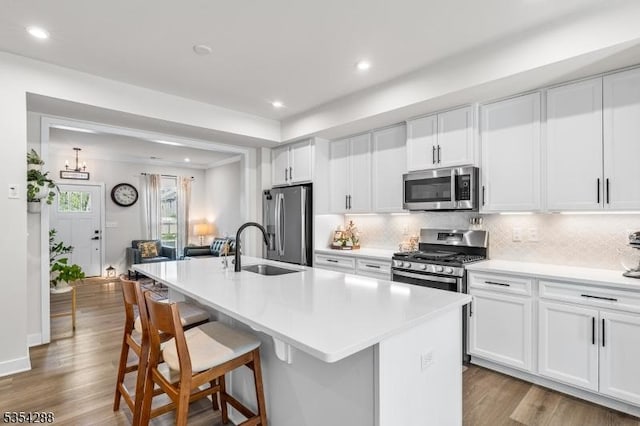 kitchen with appliances with stainless steel finishes, a sink, wood finished floors, backsplash, and a center island with sink