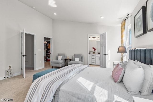 bedroom with connected bathroom, light carpet, a walk in closet, baseboards, and vaulted ceiling