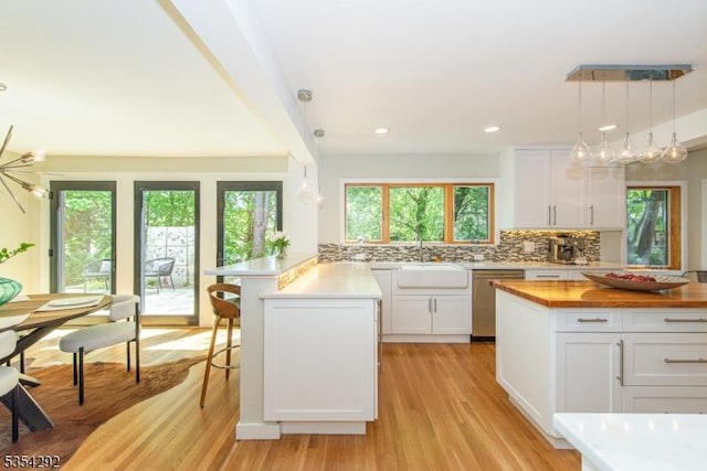 kitchen with a peninsula, white cabinetry, a sink, light wood-style flooring, and dishwasher