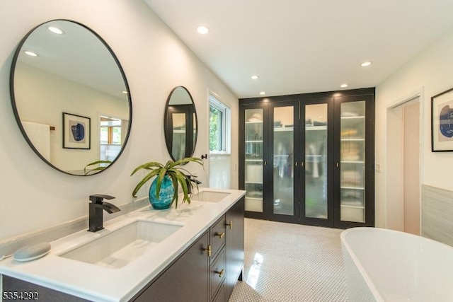 full bath featuring a freestanding bath, a sink, double vanity, french doors, and recessed lighting