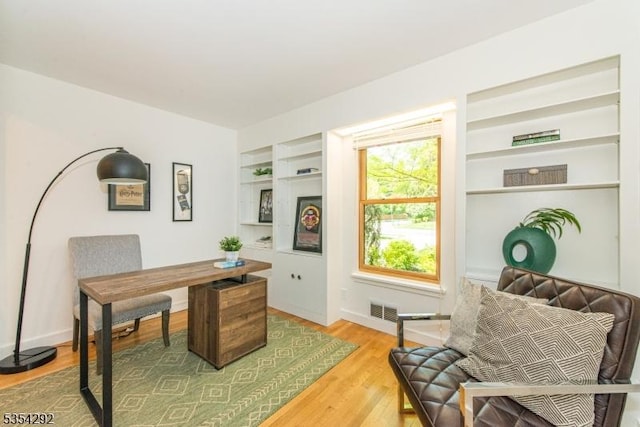 home office featuring visible vents, built in features, and light wood-type flooring