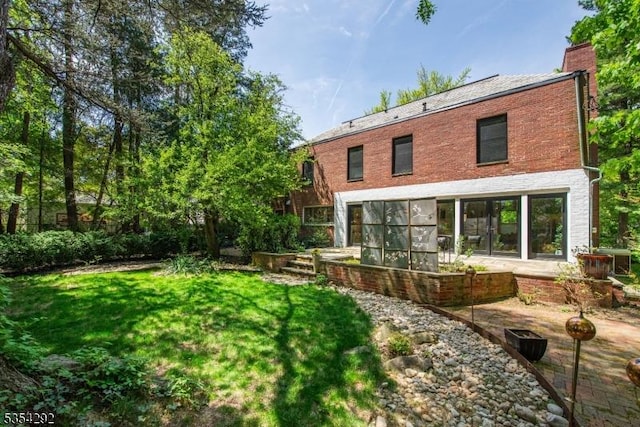 back of property with a yard, a patio, a chimney, and brick siding