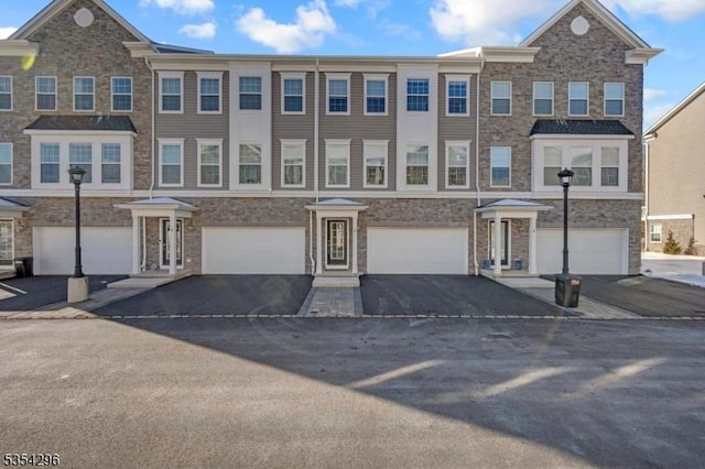 view of property featuring an attached garage, driveway, and stone siding