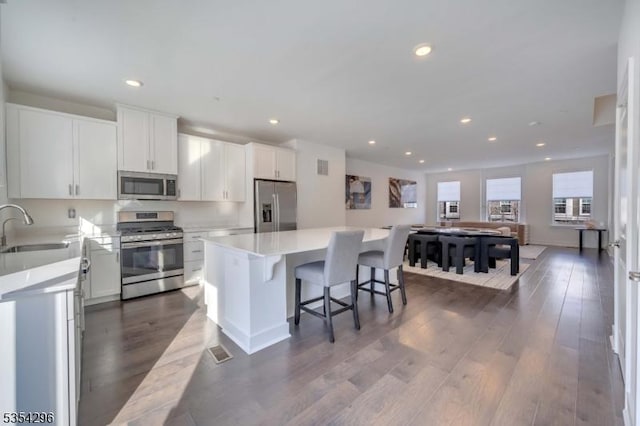 kitchen featuring a kitchen island, a sink, light countertops, stainless steel appliances, and dark wood-type flooring