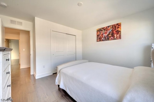 bedroom with baseboards, visible vents, wood finished floors, and a closet