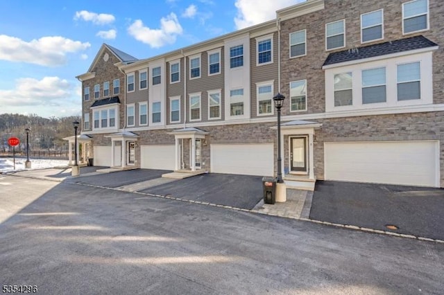 view of property with an attached garage, driveway, and stone siding