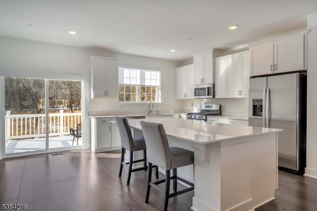 kitchen with a kitchen island, light countertops, a sink, dark wood finished floors, and appliances with stainless steel finishes