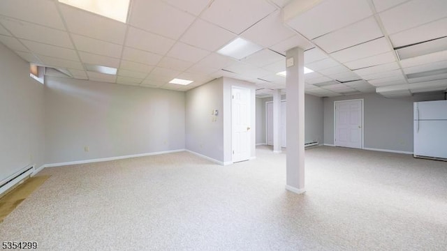 below grade area featuring freestanding refrigerator, a paneled ceiling, a baseboard radiator, baseboards, and a baseboard heating unit