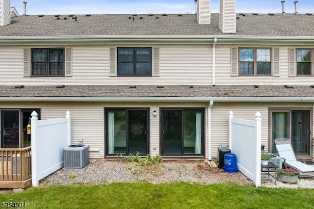 back of property with a chimney, central AC, fence, and roof with shingles