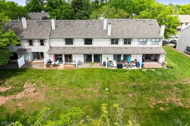 rear view of property featuring a patio, a chimney, a yard, and view of wooded area