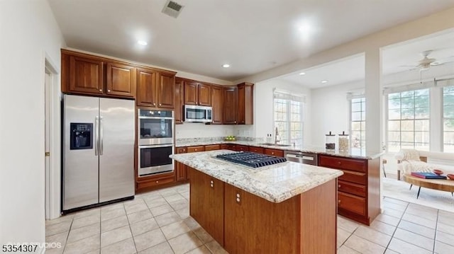 kitchen with light tile patterned flooring, light stone countertops, a center island, stainless steel appliances, and visible vents