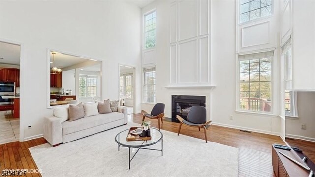 living room featuring an inviting chandelier, a towering ceiling, wood finished floors, baseboards, and a fireplace with flush hearth