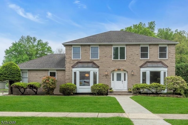 view of front of house with a front lawn, brick siding, and a shingled roof