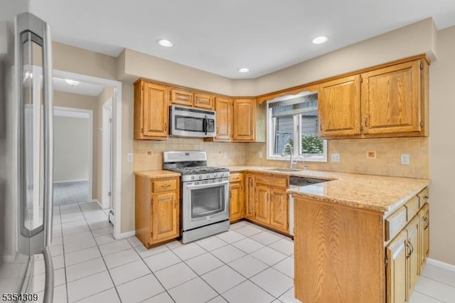 kitchen featuring stainless steel appliances, a sink, a peninsula, decorative backsplash, and baseboards