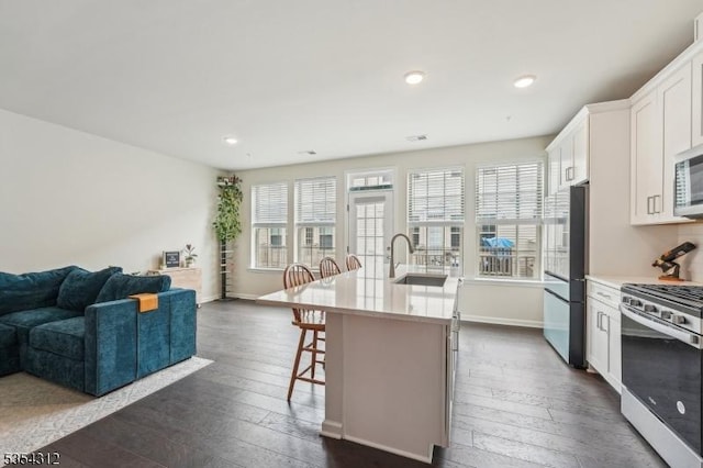 kitchen featuring a kitchen island with sink, open floor plan, a breakfast bar area, dark wood finished floors, and stainless steel appliances