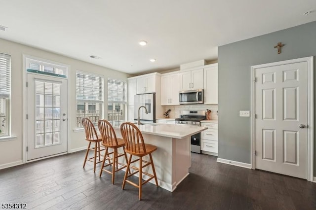 kitchen with visible vents, dark wood-style flooring, a kitchen island with sink, a breakfast bar, and stainless steel appliances