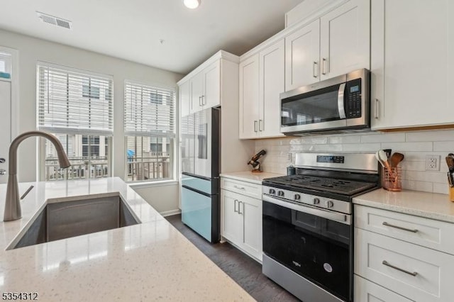 kitchen featuring visible vents, light stone countertops, a sink, white cabinets, and stainless steel appliances