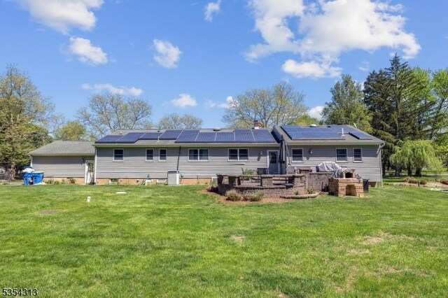 back of house with roof mounted solar panels and a yard