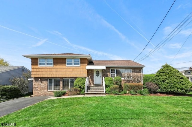 split level home with brick siding, aphalt driveway, and a front lawn