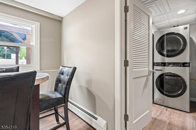 clothes washing area with baseboard heating, light wood-style floors, stacked washer and clothes dryer, and laundry area