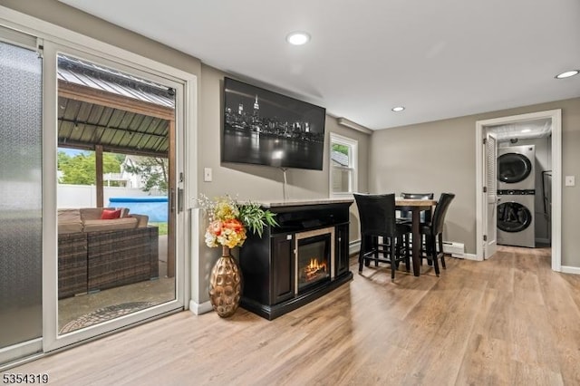 living room featuring light wood-type flooring, a glass covered fireplace, stacked washer / dryer, and baseboard heating