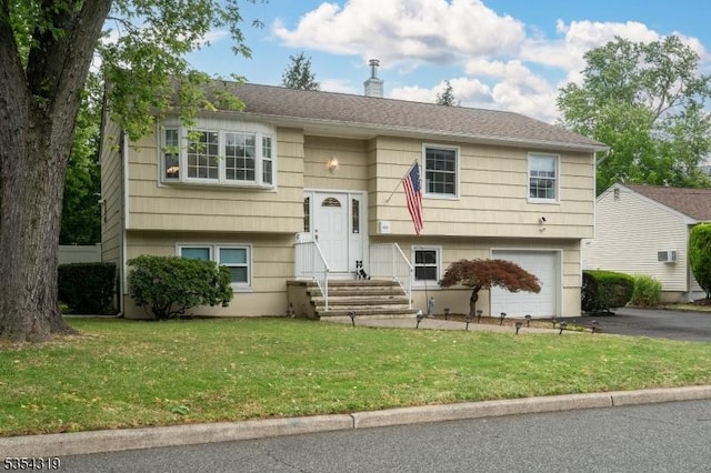 raised ranch featuring an attached garage, a front lawn, entry steps, and aphalt driveway