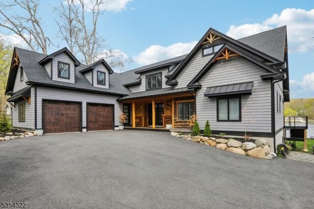 view of front of house with roof with shingles, a standing seam roof, a porch, and driveway