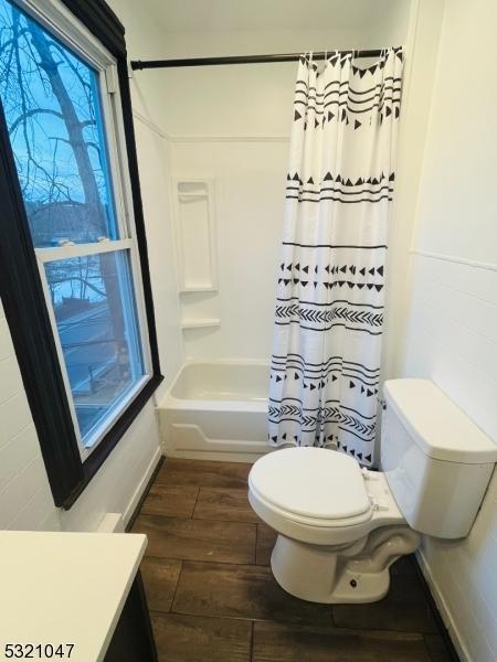 bathroom featuring vanity, toilet, shower / bathtub combination with curtain, baseboards, and wood finished floors