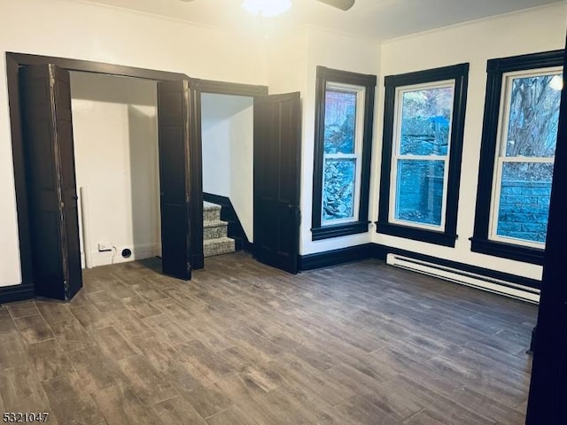 unfurnished room featuring wood finished floors, a ceiling fan, a baseboard heating unit, and stairway