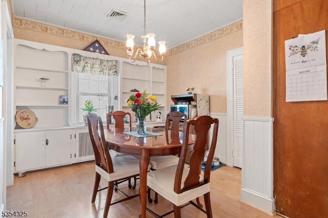 dining space featuring a notable chandelier, light wood finished floors, a wainscoted wall, visible vents, and ornamental molding