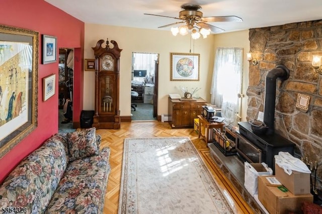 living room featuring a wood stove, a ceiling fan, and baseboard heating