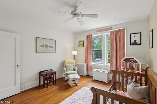 bedroom with radiator heating unit, wood finished floors, a crib, and a ceiling fan