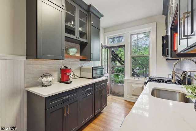kitchen with light countertops, light wood-type flooring, a sink, tasteful backsplash, and glass insert cabinets