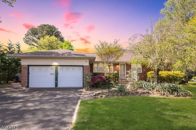 ranch-style home with brick siding, a garage, a front lawn, and aphalt driveway
