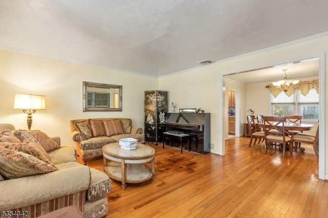 living area featuring visible vents, a chandelier, ornamental molding, and light wood finished floors