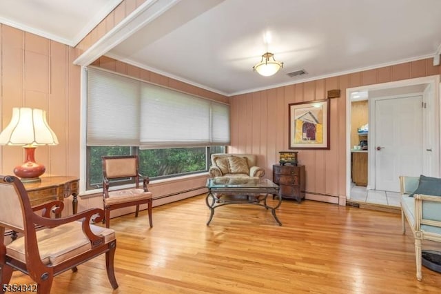 living area with a baseboard heating unit, visible vents, ornamental molding, and light wood-type flooring
