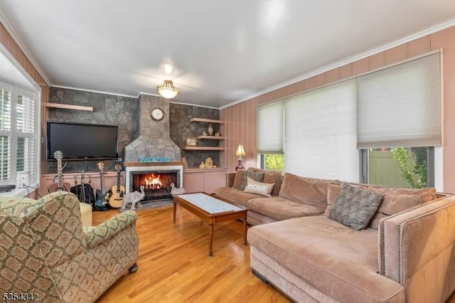 living room with crown molding, a stone fireplace, and wood finished floors
