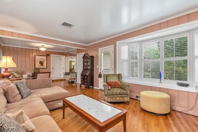 living room with visible vents, wood walls, wood finished floors, a baseboard heating unit, and ornamental molding