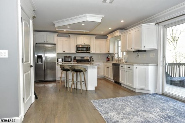 kitchen with a breakfast bar area, a kitchen island, appliances with stainless steel finishes, white cabinets, and dark wood-style floors