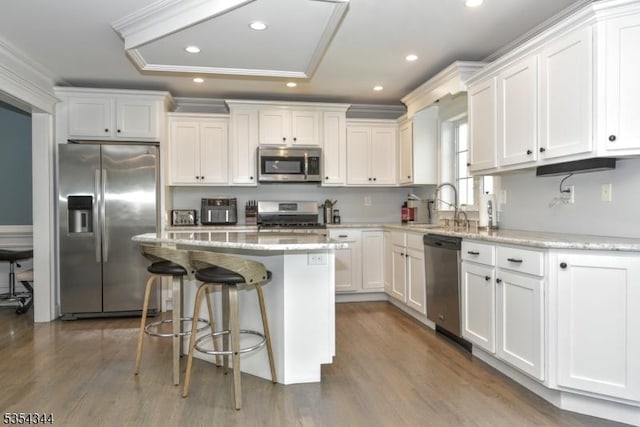 kitchen featuring appliances with stainless steel finishes, a sink, white cabinetry, wood finished floors, and a kitchen island