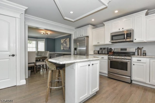 kitchen with stainless steel appliances, white cabinetry, ornamental molding, and wood finished floors