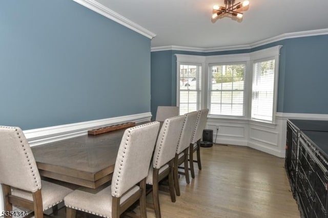 dining area featuring crown molding, an inviting chandelier, wainscoting, a decorative wall, and wood finished floors