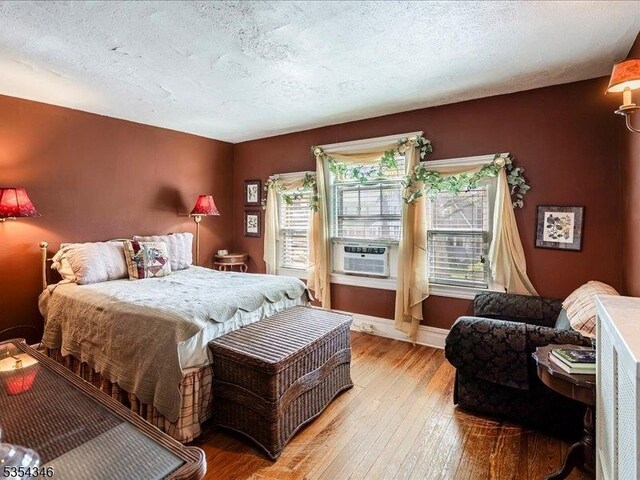 bedroom with wood-type flooring, a textured ceiling, baseboards, and cooling unit