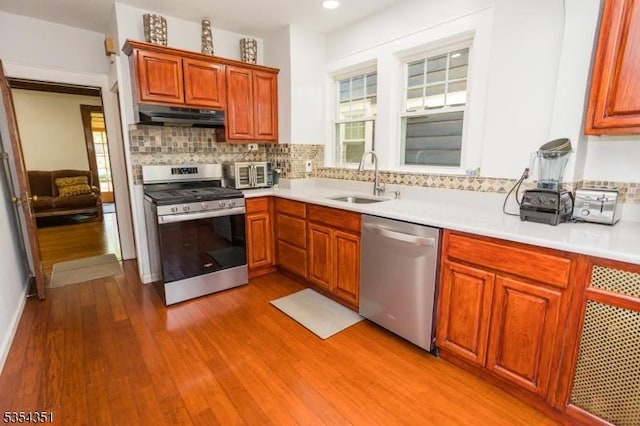 kitchen featuring under cabinet range hood, a sink, light wood-style flooring, appliances with stainless steel finishes, and backsplash