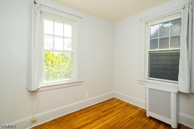 spare room featuring radiator heating unit, baseboards, and wood finished floors