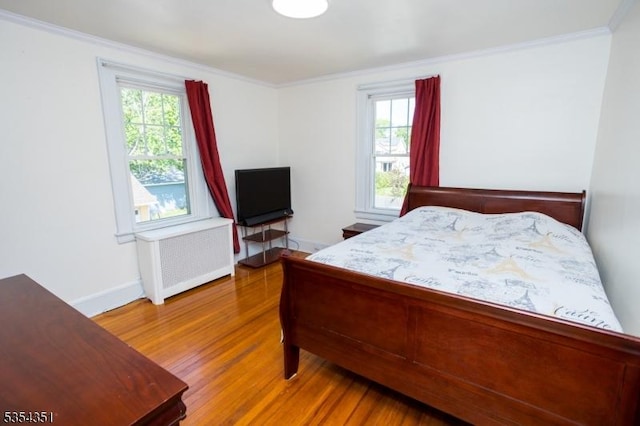 bedroom with baseboards, ornamental molding, radiator heating unit, and wood finished floors