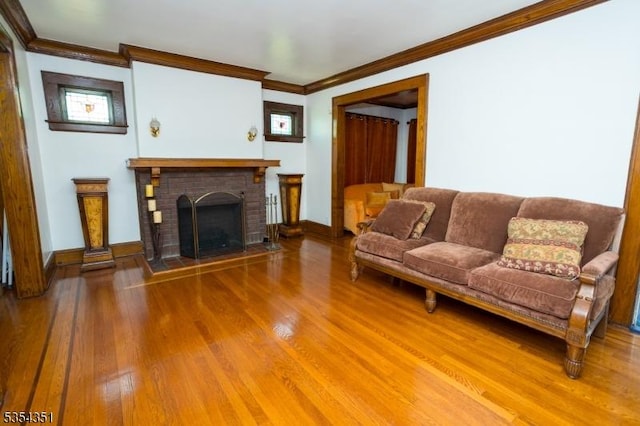 living area with baseboards, ornamental molding, a brick fireplace, and wood finished floors