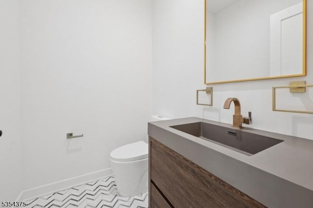 half bathroom with vanity, baseboards, and toilet