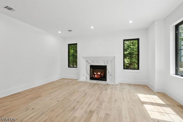 unfurnished living room featuring visible vents, light wood-style floors, baseboards, recessed lighting, and a premium fireplace